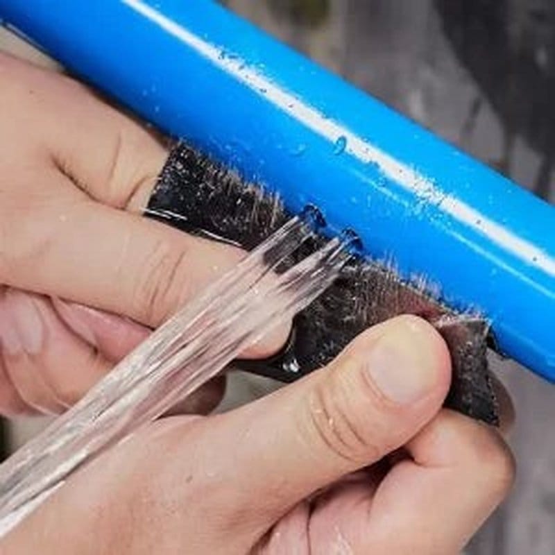 Ruka drži crnu samolepljivu traku za zaptivanje ispred jakog mlaza vode koji prska na sve strane
